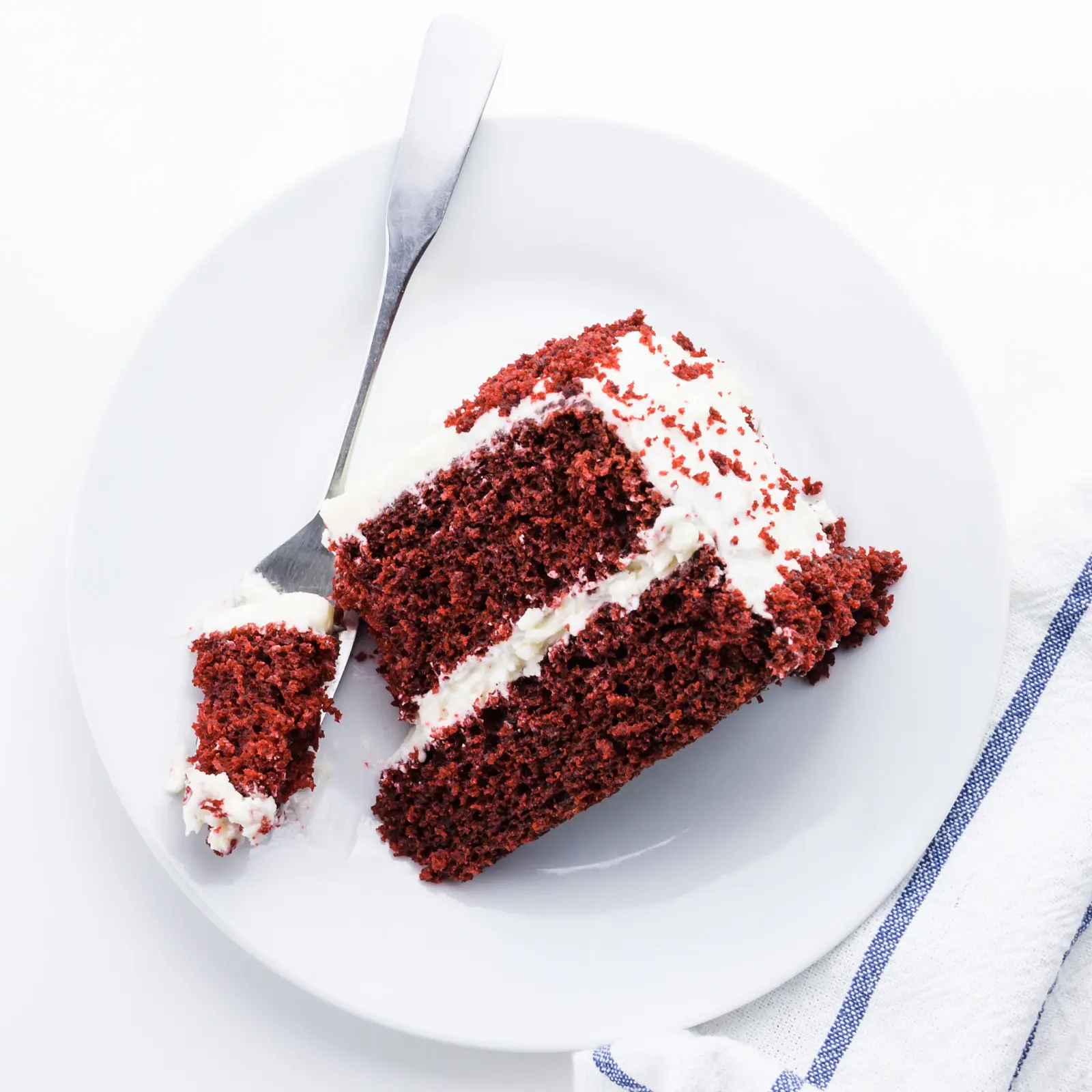 A slice of red velvet cake on a plate with a fork holding a mouthful beside it.