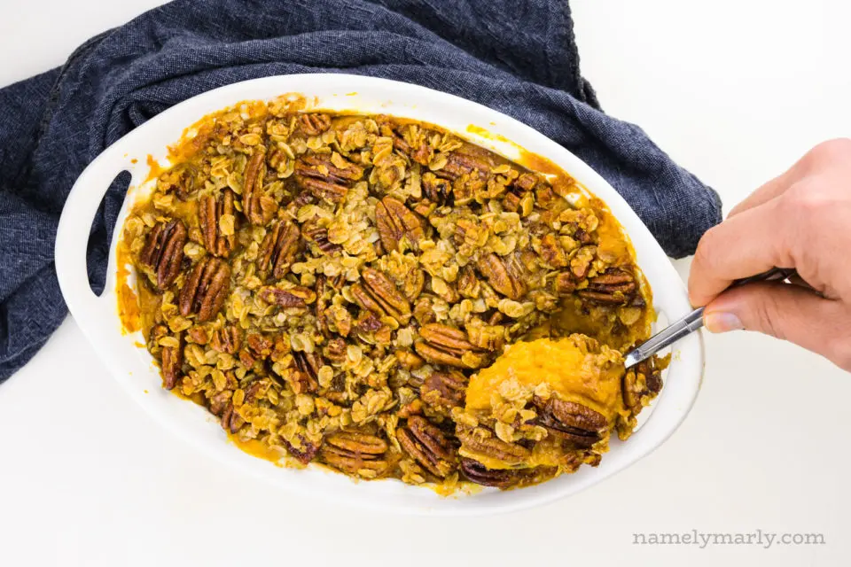 Looking down on a casserole dish with a hand spooning out some of the sweet potato casserole.