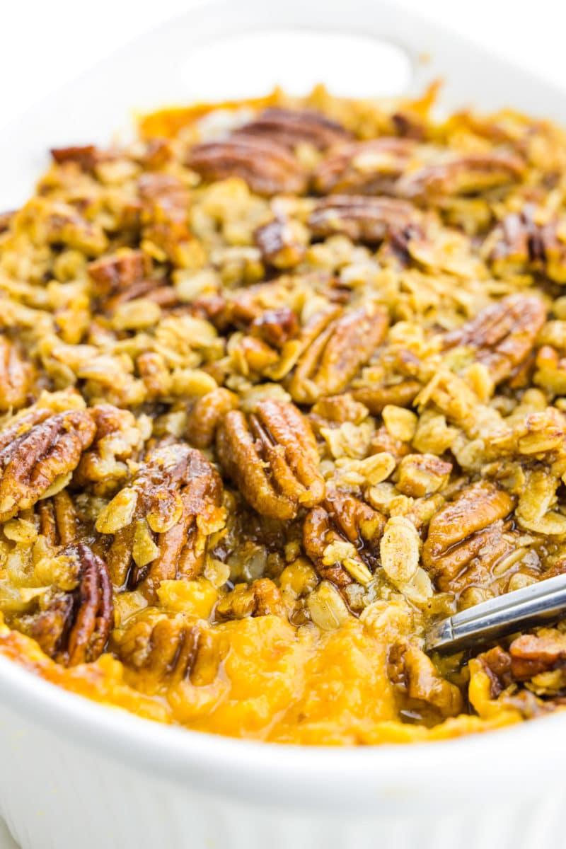 A casserole dish holds sweet potato casserole with a spoon scooping some out.