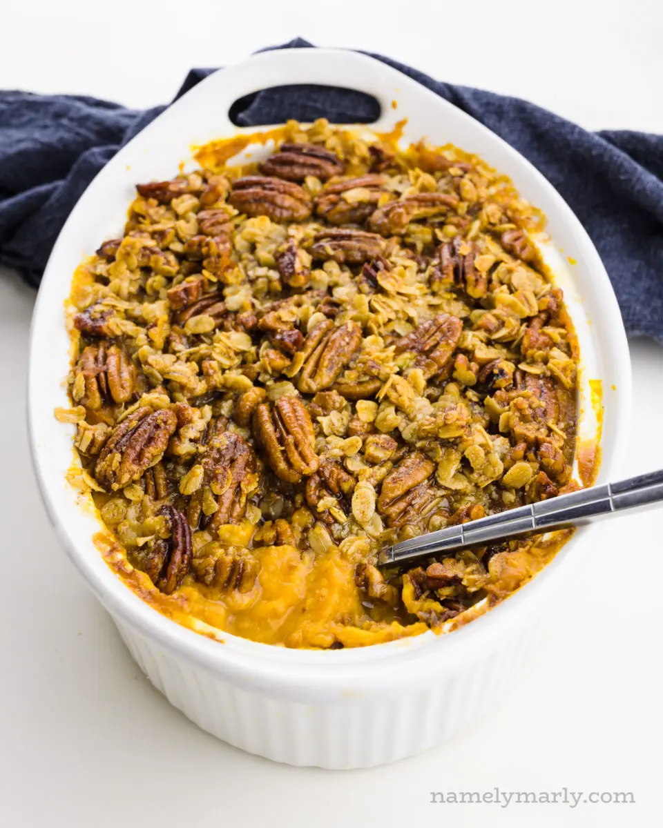 A casserole holds sweet potato casserole and a spoon has dished out some of it.