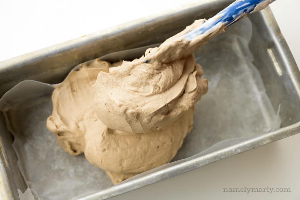 Whipped chocolate topping is being spread into a prepared pan.