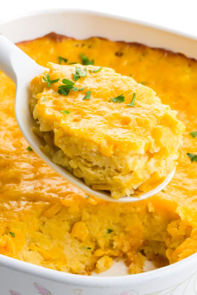 A spoonful of vegan corn casserole hovers over the rest of the casserole dish.