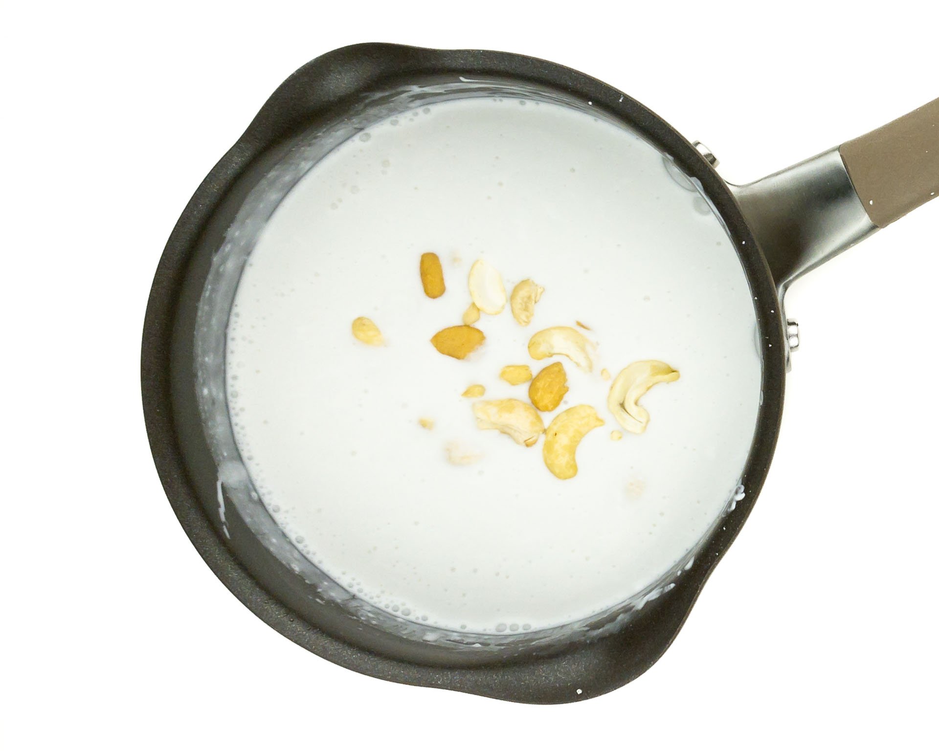 A saucepan holds coconut milk with cashews.