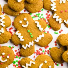 Several decorated gingerbread cookies are on a white countertop with sprinkles between them.