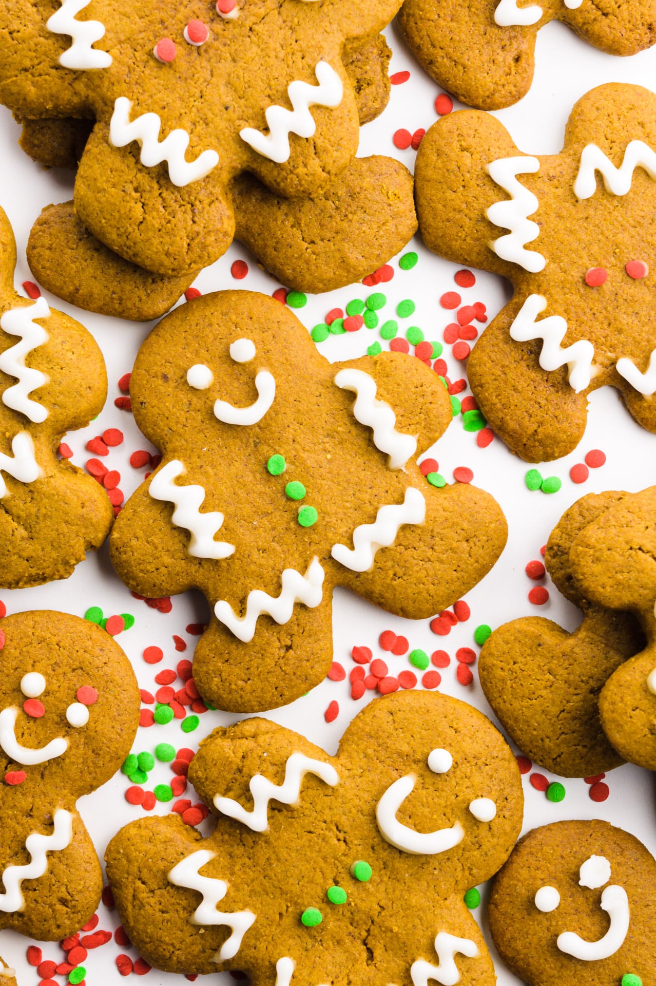 Several decorated gingerbread cookies are on a white countertop with sprinkles between them.