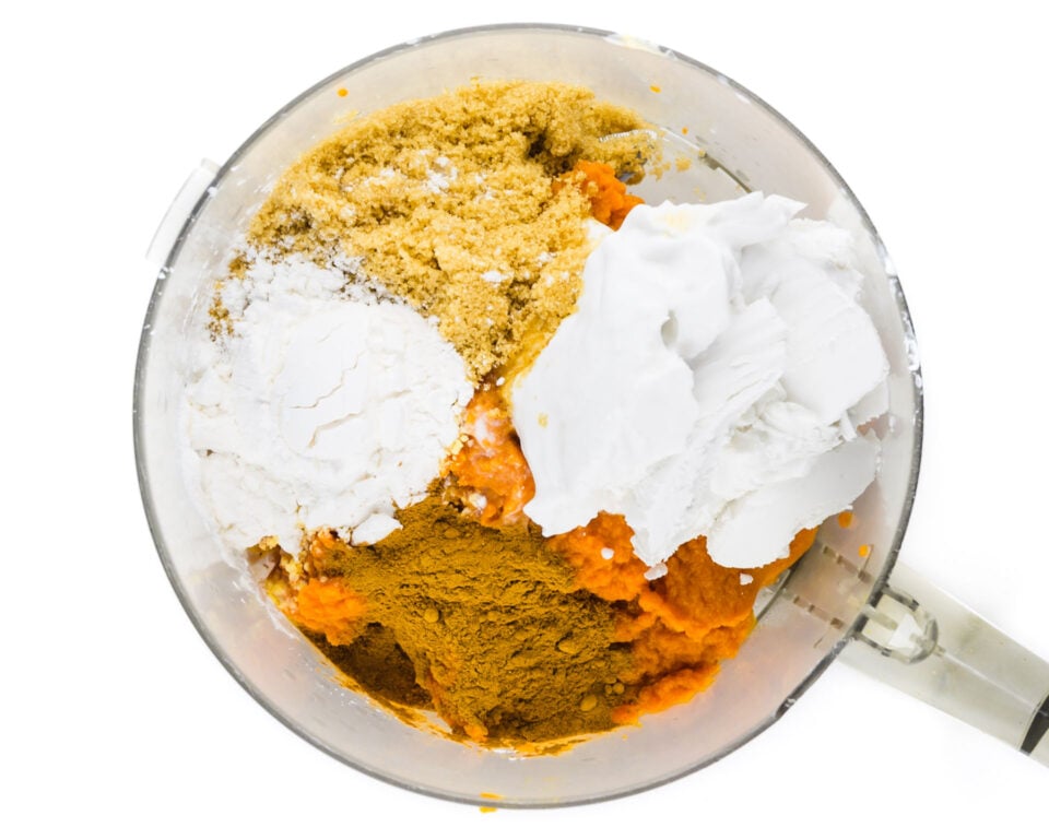 Ingredients like coconut milk, brown sugar, and spices are in a food processor bowl.