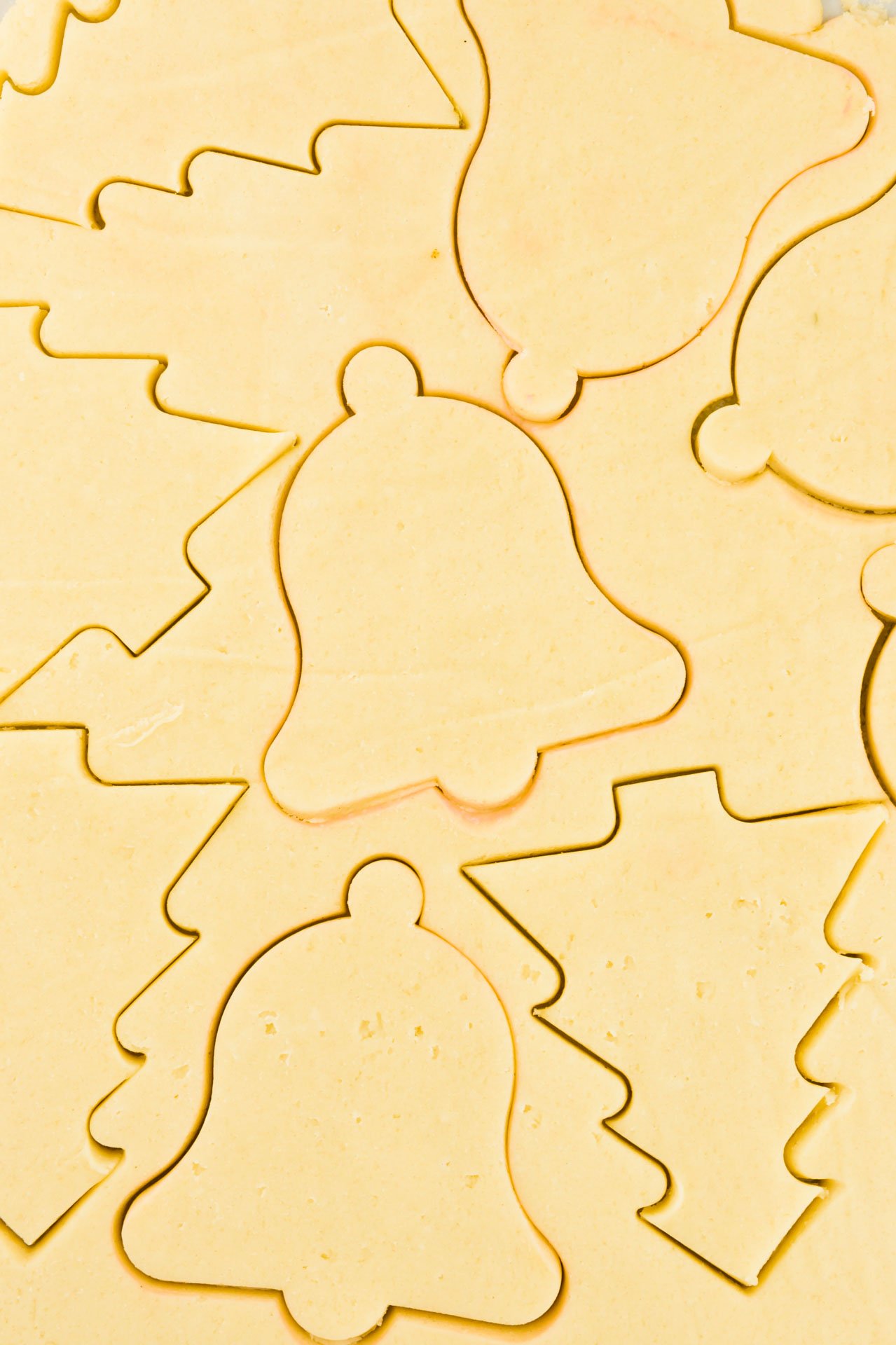 Rolled cookie dough has been cut into shapes using Christmas cookie cutters.