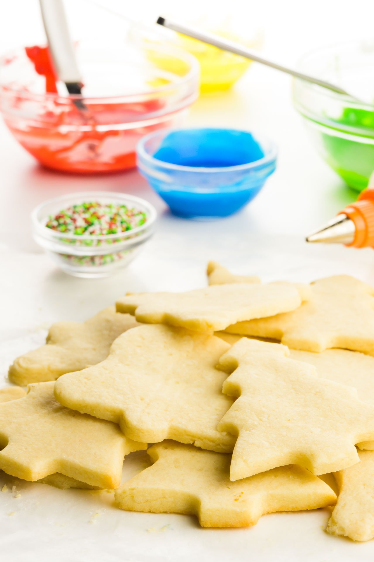 Several unfrosted cookies sit in front of containers of colorful frosting and cookie decorations.