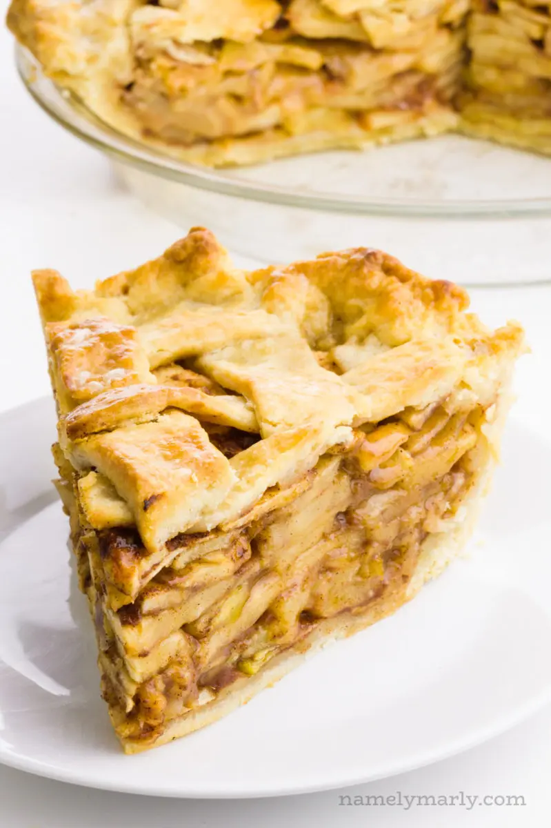 A slice of apple pie with lattice top sits in front of the rest of the pie.