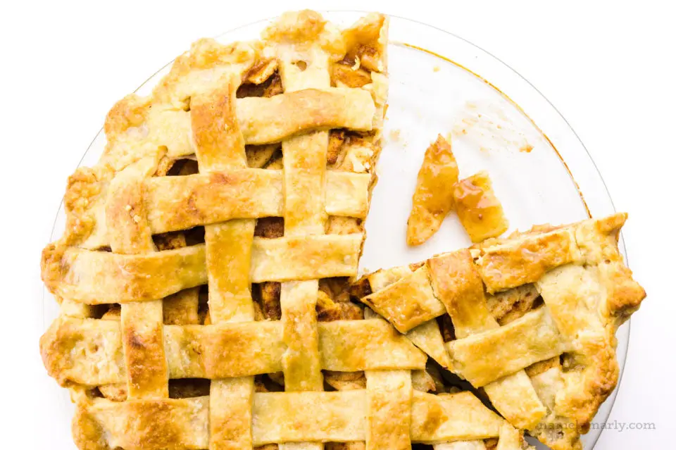 Looking down on a lattice-topped pie with a slice taken out and some apple slices in the bottom of the pan.