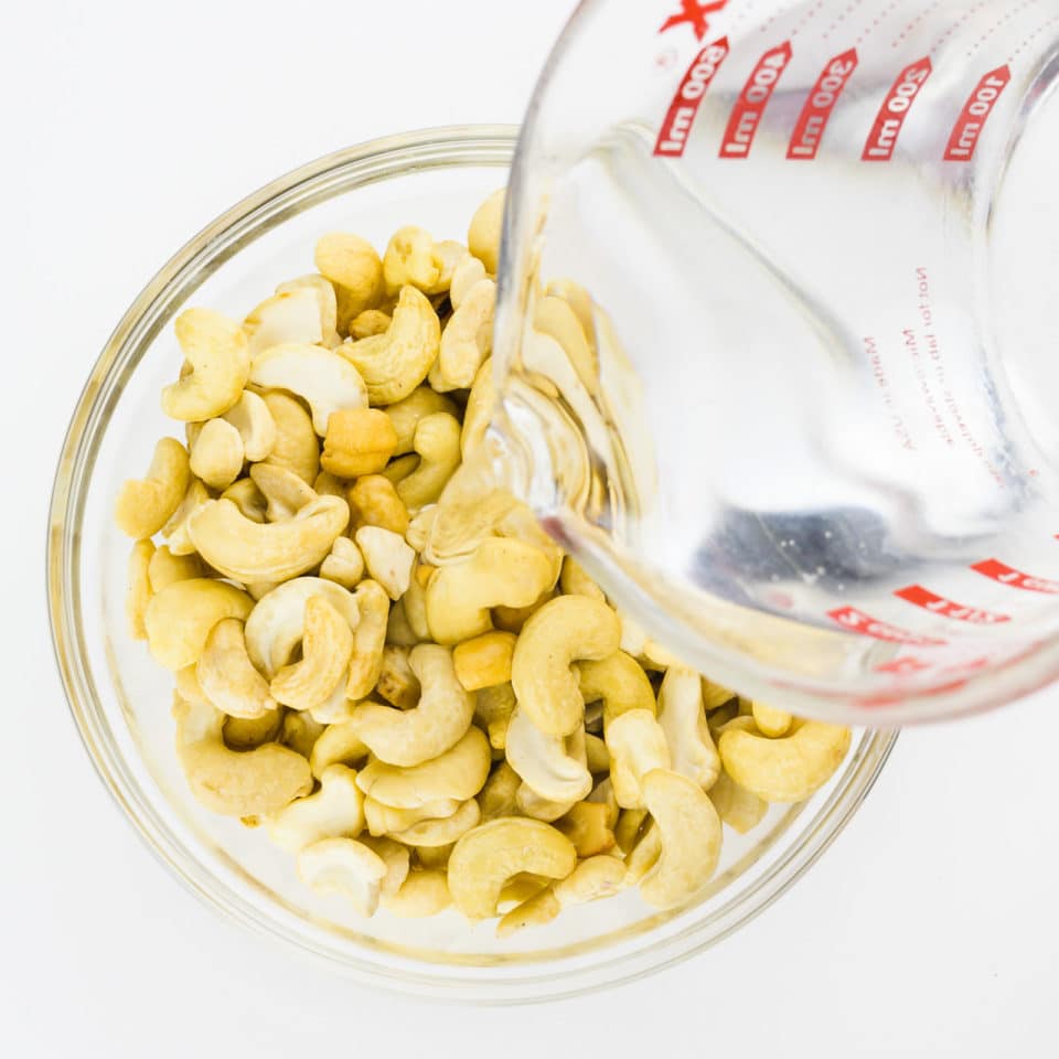 A pyrex measuring cup full of hot water is being poured over raw cashews.
