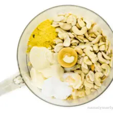 Cashews and other ingredients are in the bowl of a food processor.