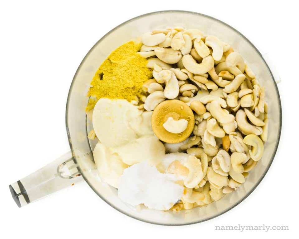 Cashews and other ingredients are in the bowl of a food processor.