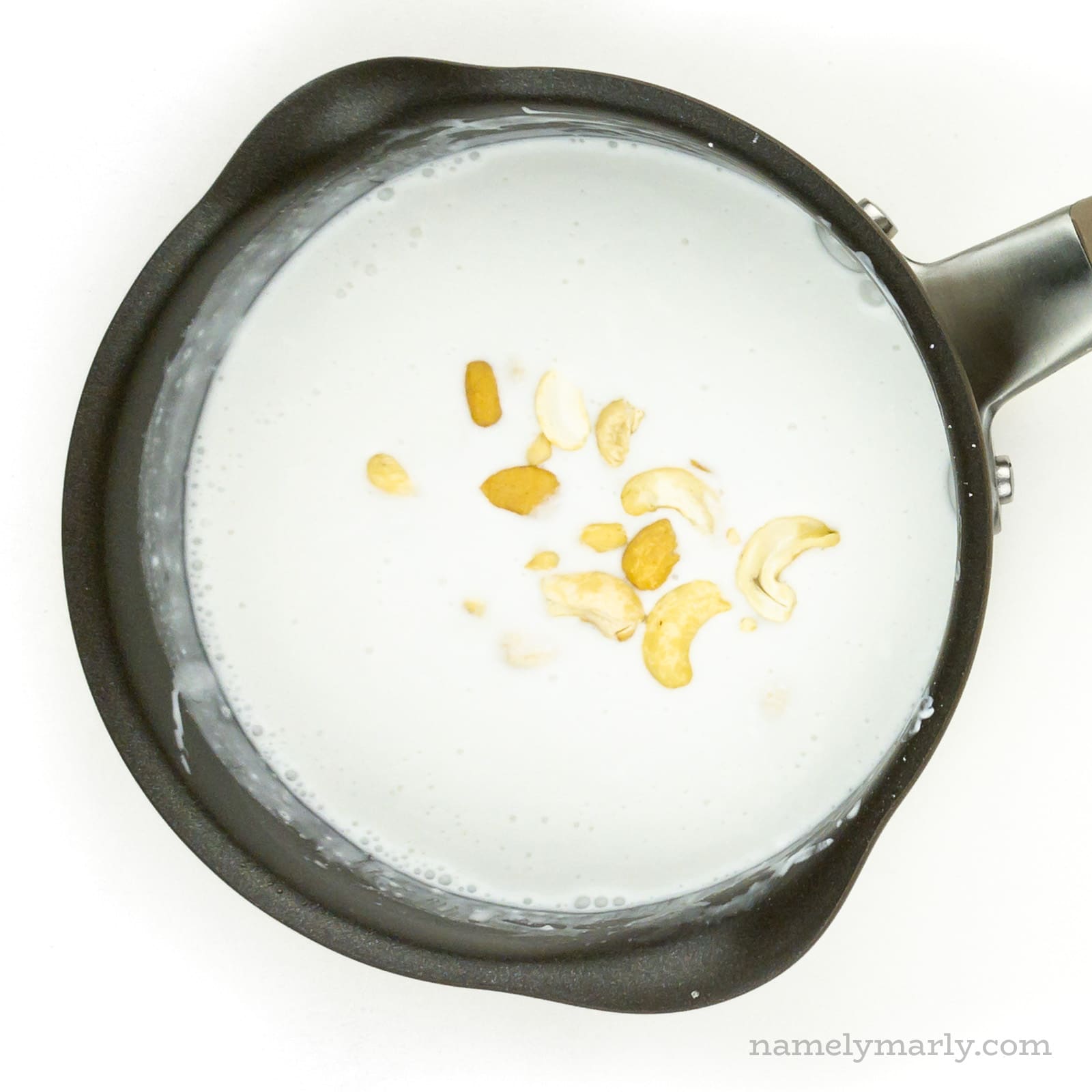 A saucepan holds coconut milk with cashews.