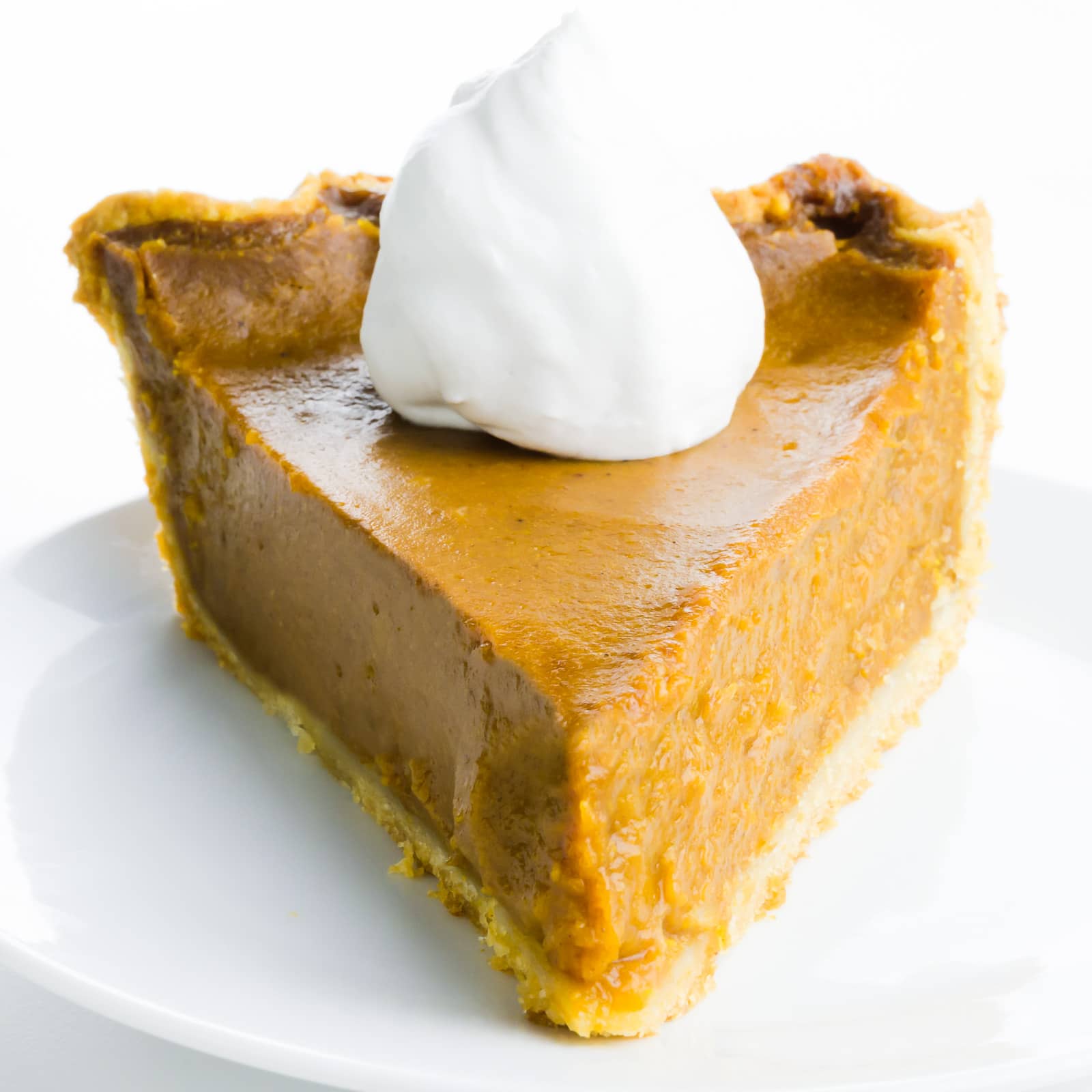 A slice of pumpkin pie with whipped cream sits on a plate.