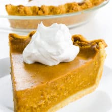 A slice of vegan pumpkin pie with a dollop of whipped cream sits in front of the rest of the pie.