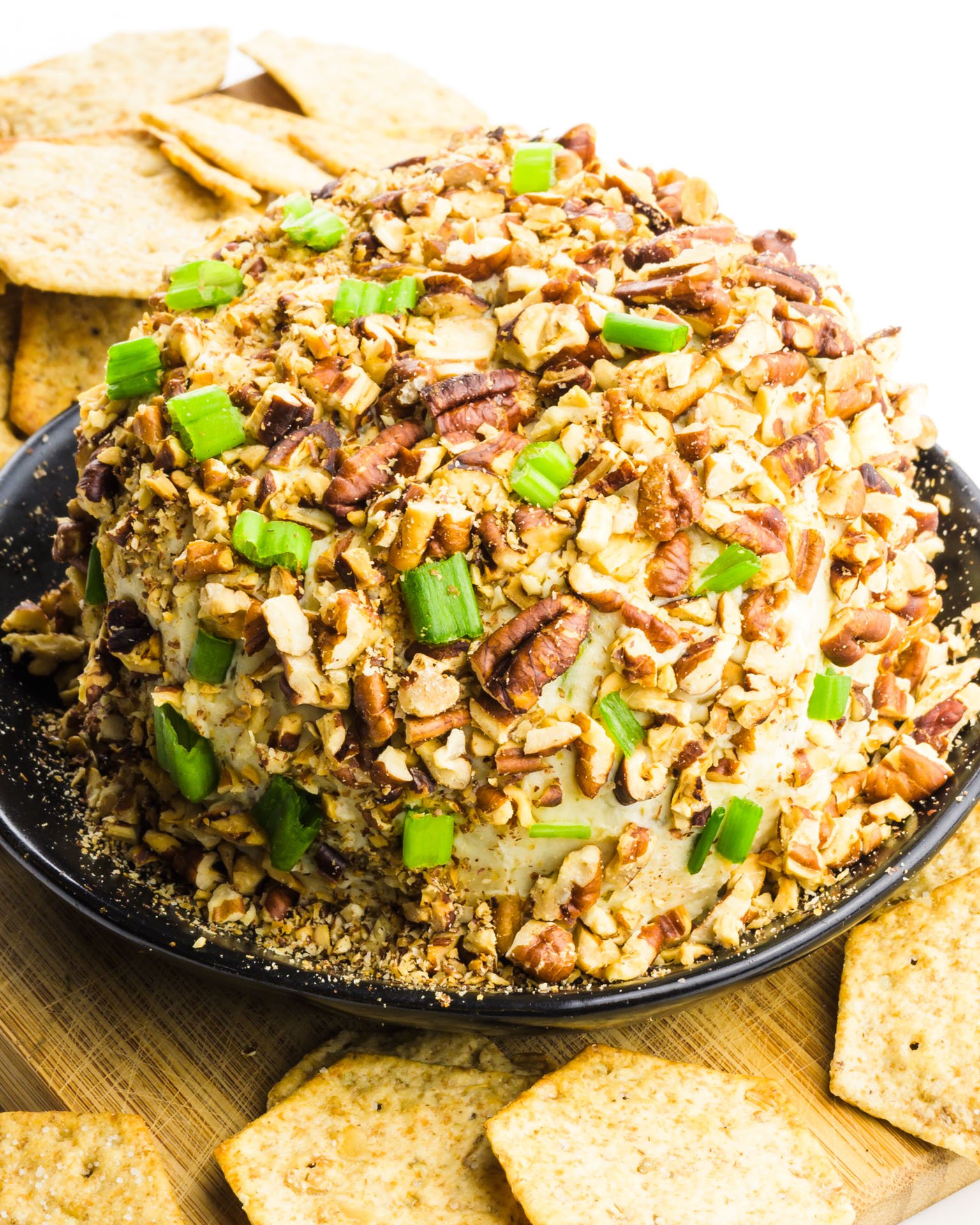 A cheeseball sits on a plate with crackers around it.