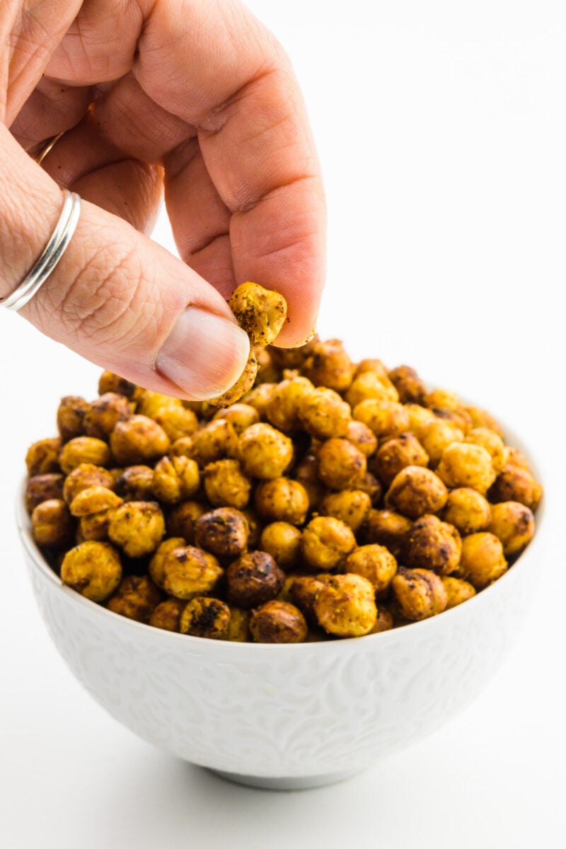 A hand reaches in grabs some air fryer chickpeas from a bowl.