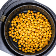 A hand holds an air fryer basket full of spiced chickpeas.