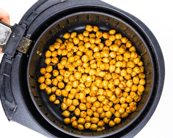 A hand holds an air fryer basket full of spiced chickpeas.