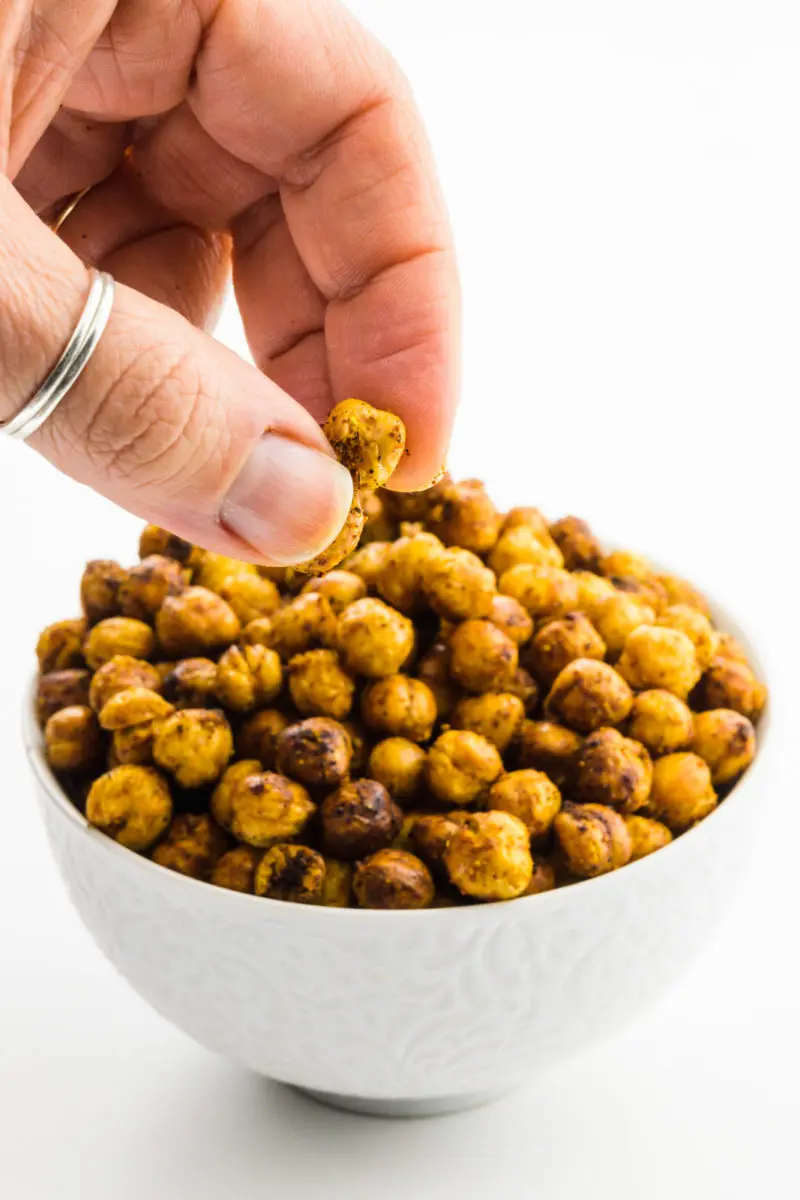 A hand reaches in grabs some air fryer chickpeas from a bowl.