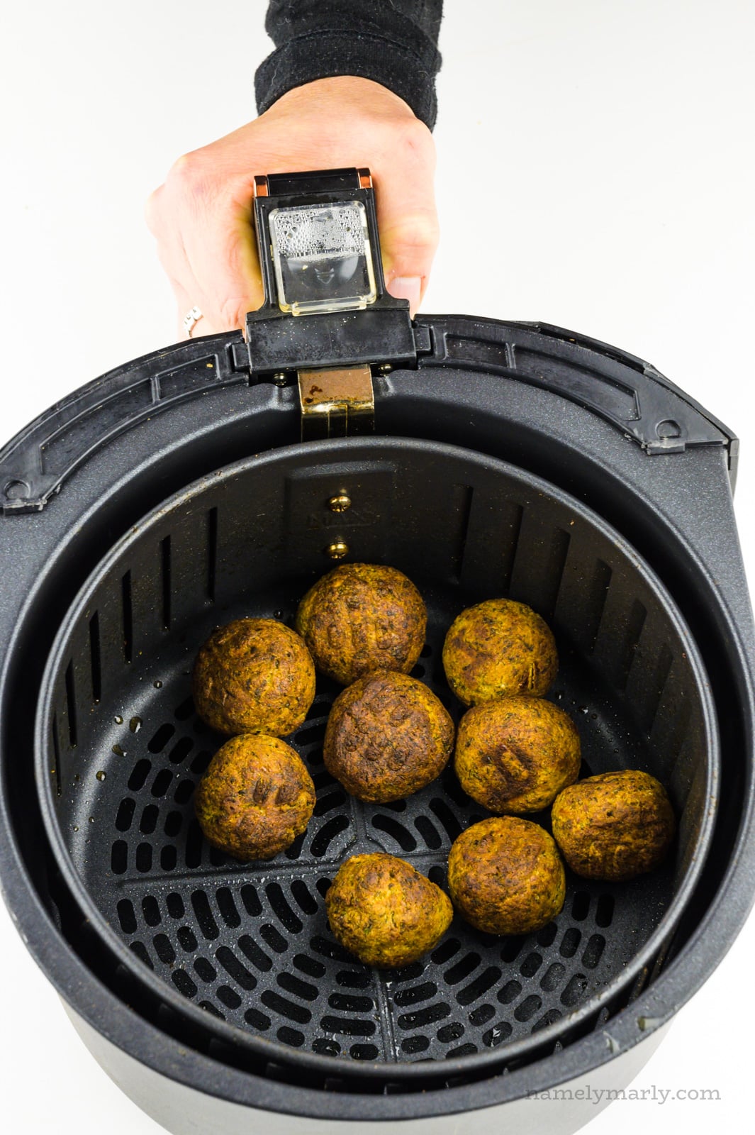 Crispy brown air fried falafel are in an air fryer basket.
