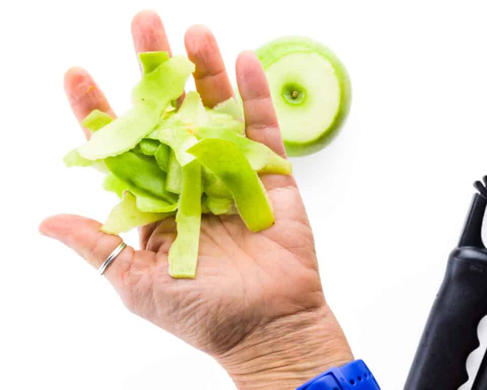 A hand holds several green apple peels.