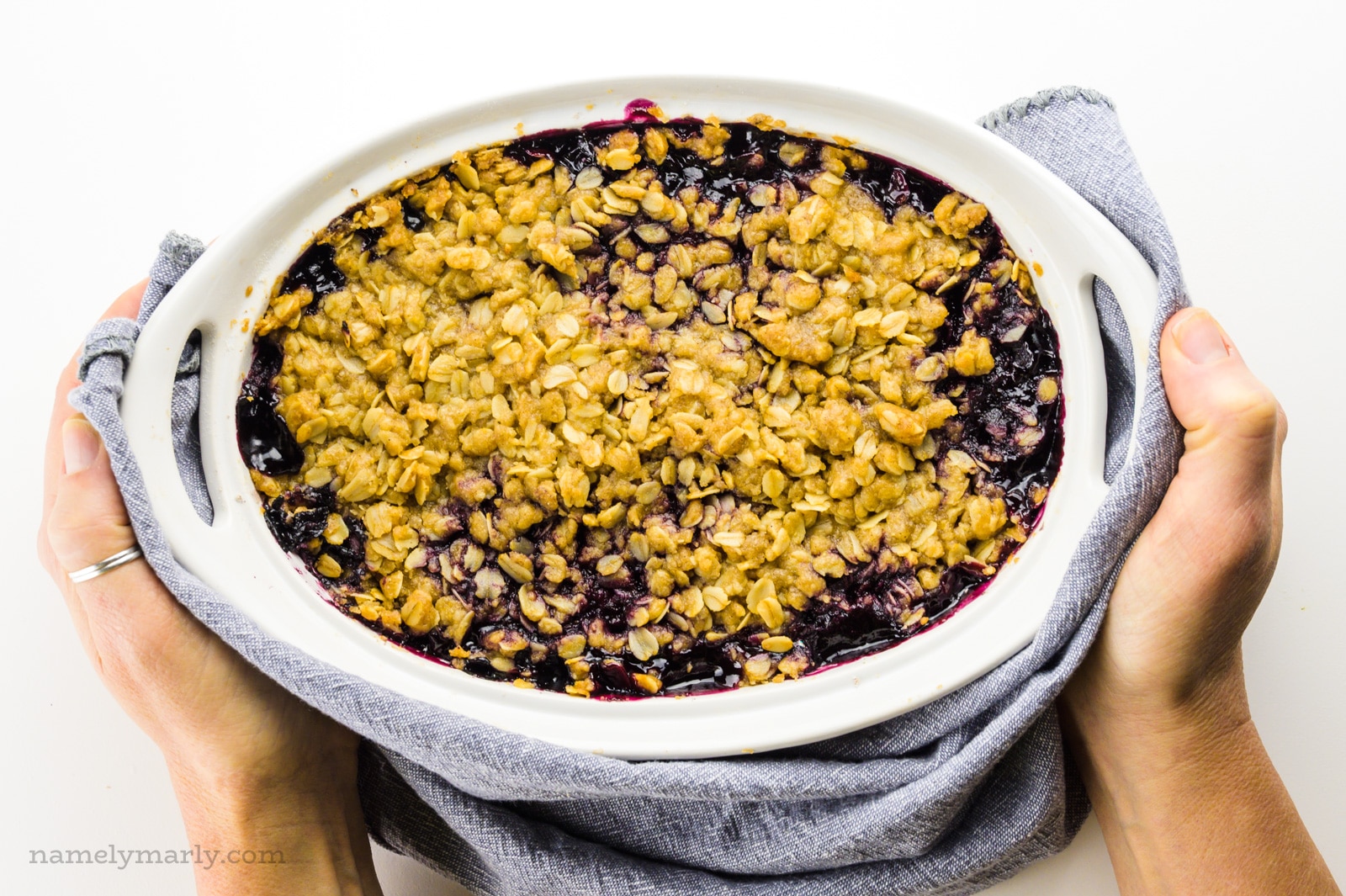 Hands hold a towel around a freshly baked batch of blueberry crumble.