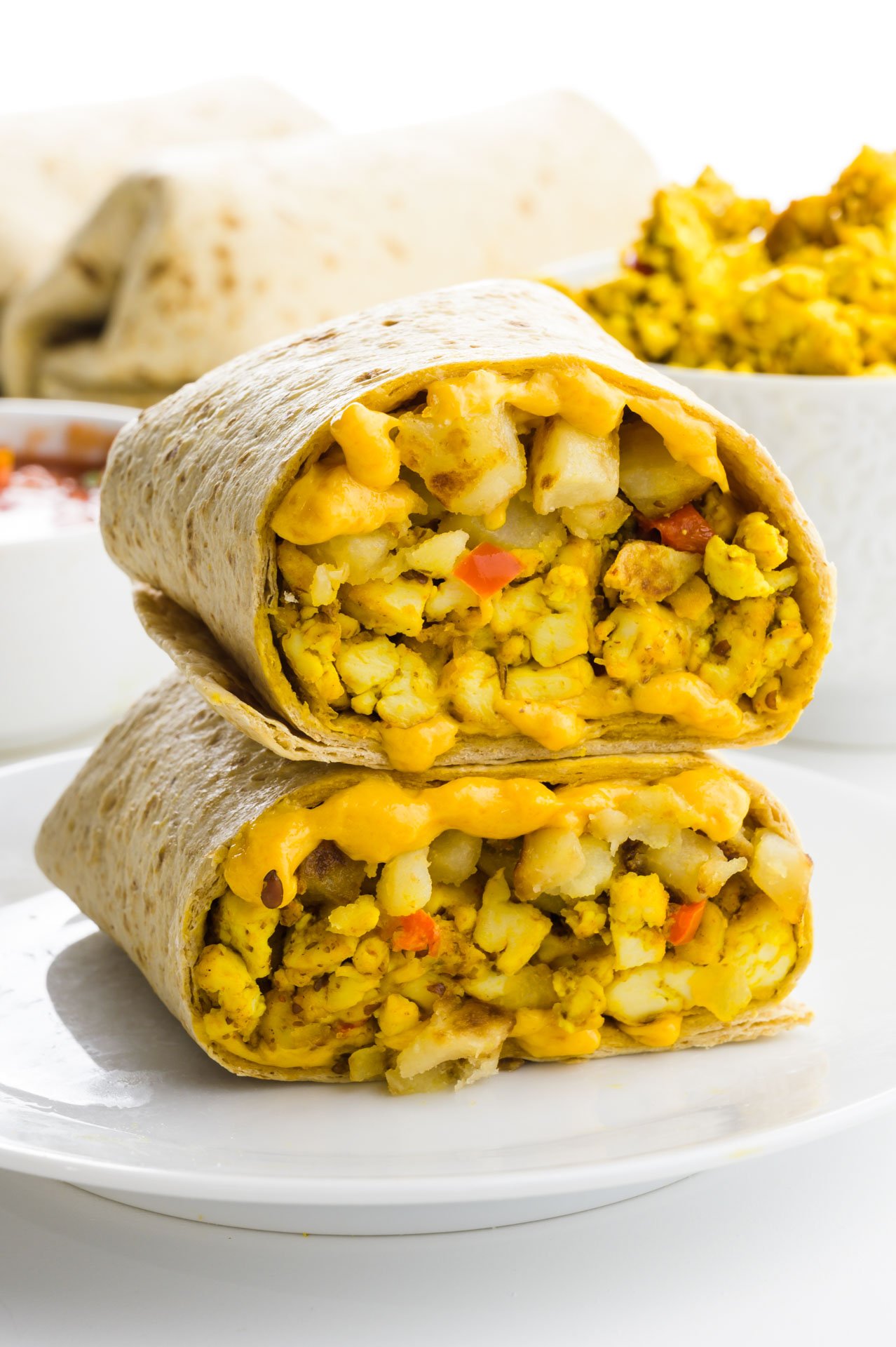 Two halves of a burrito are stacked on top of each other, with more ingredients behind it.