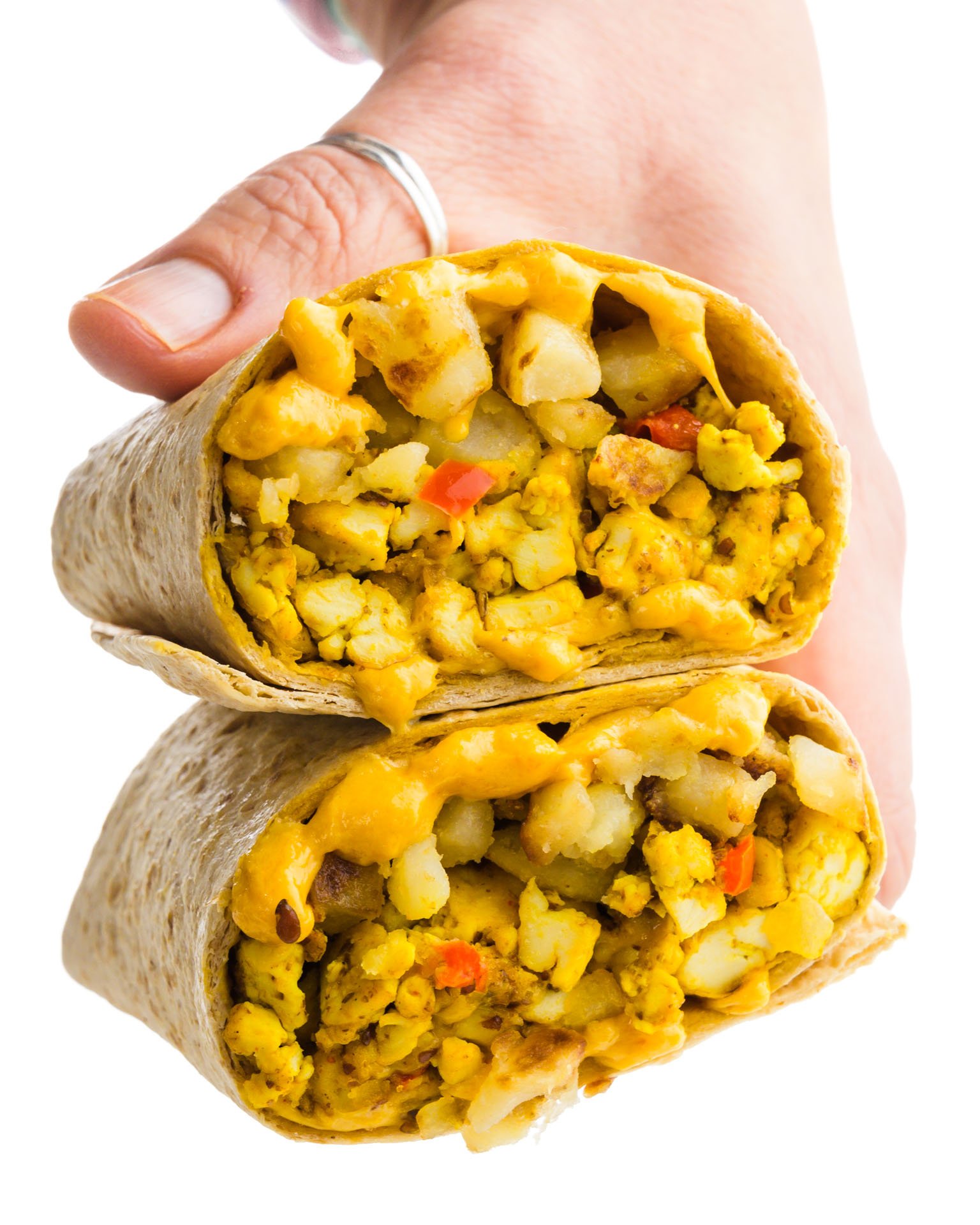A hand holds two halves of a breakfast burrito, showcasing the ingredients.