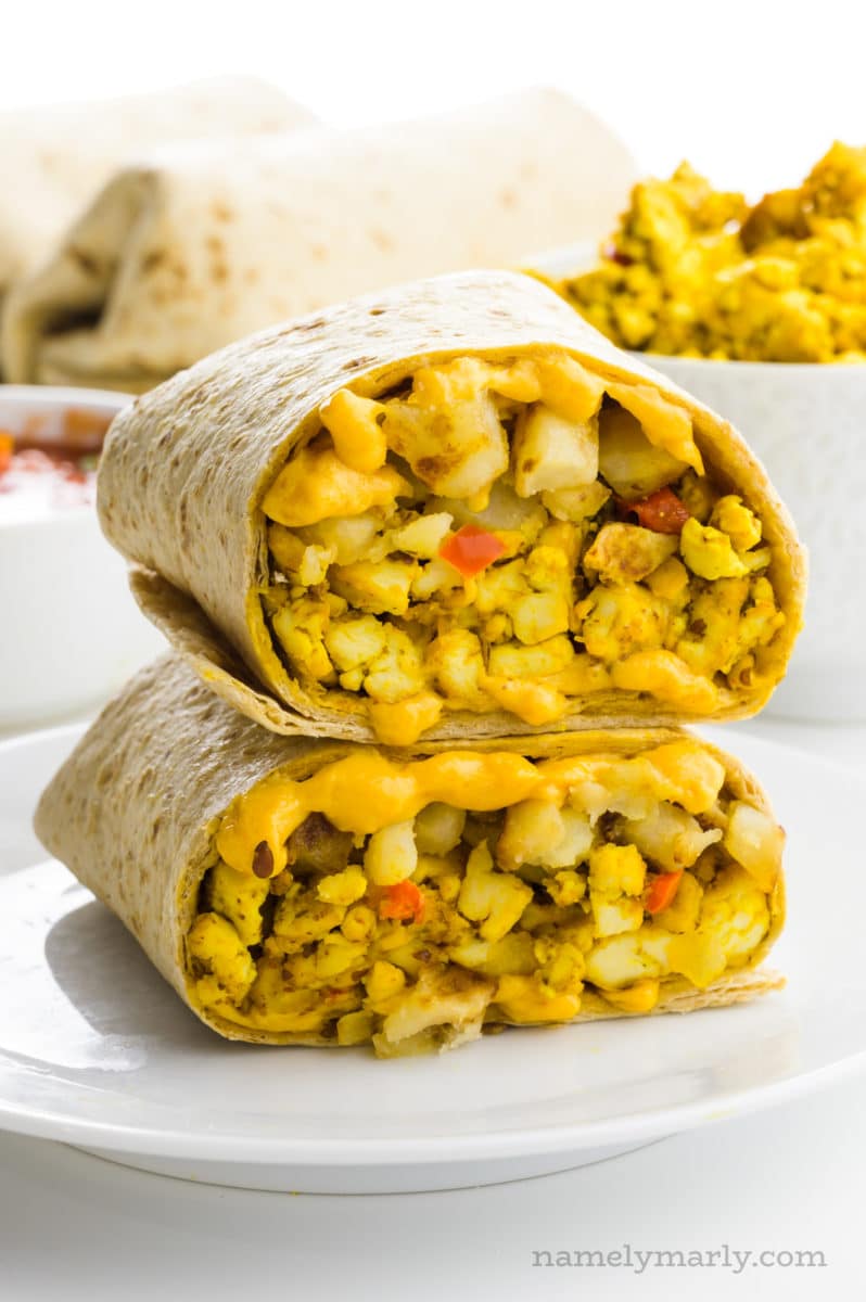 Two halves of a burrito are stacked on top of each other, with more ingredients behind it.