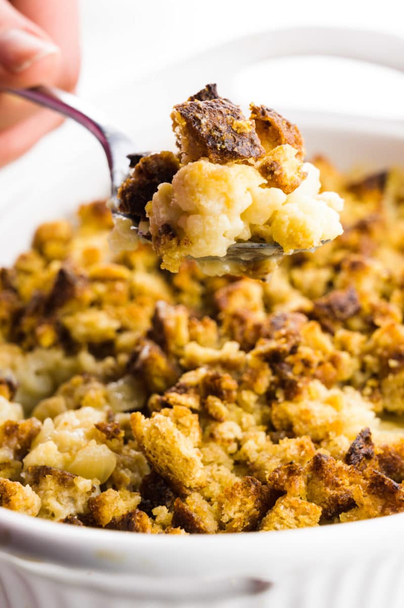 A hand holds a spoonful of cauliflower gratin, hovering over the rest of the casserole dish.