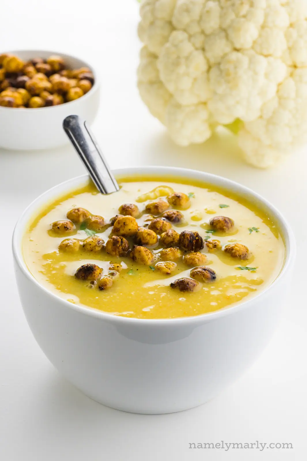 A bowl of soup with a bowl of roasted chickpeas behind it and a head of cauliflower.