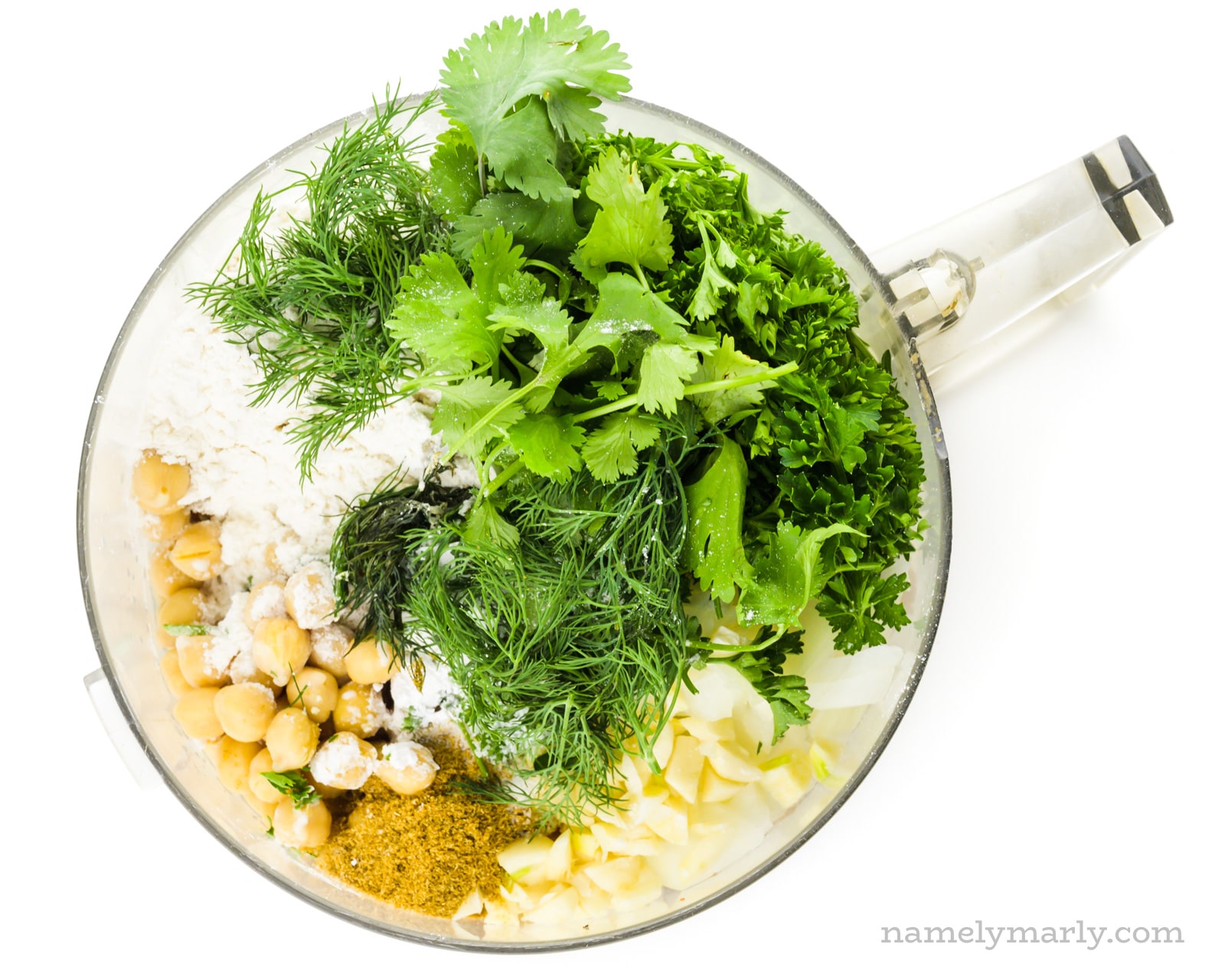 Looking down on a food processor bowl full of chickpeas, chopped onions, and fresh green herbs.