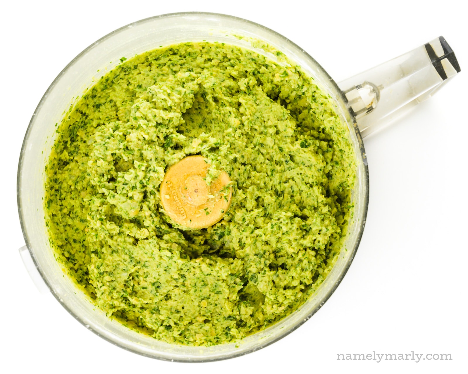 Looking down on a food processor bowl full of a green mixture of chickpeas ground with green herbs.