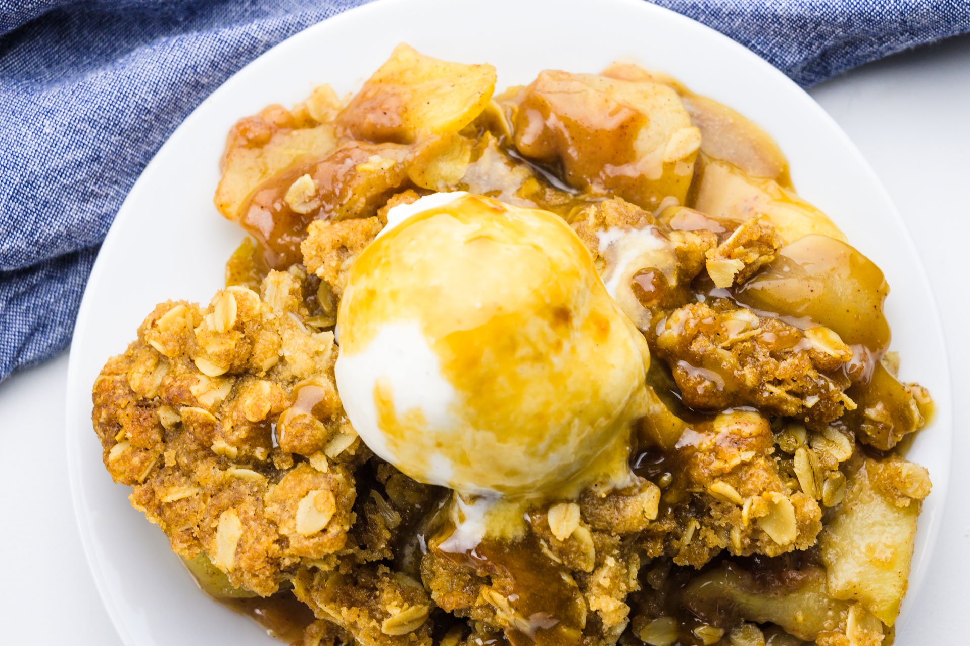 Looking down on a plate full of apple crisp with ice cream on top and covered with caramel sauce.