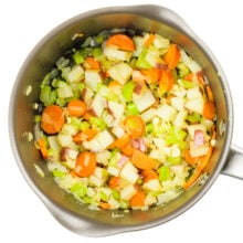 Looking down on a saucepan full of chopped onions, carrots, and celery.