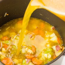 Broth is being poured into a pot full of veggies.