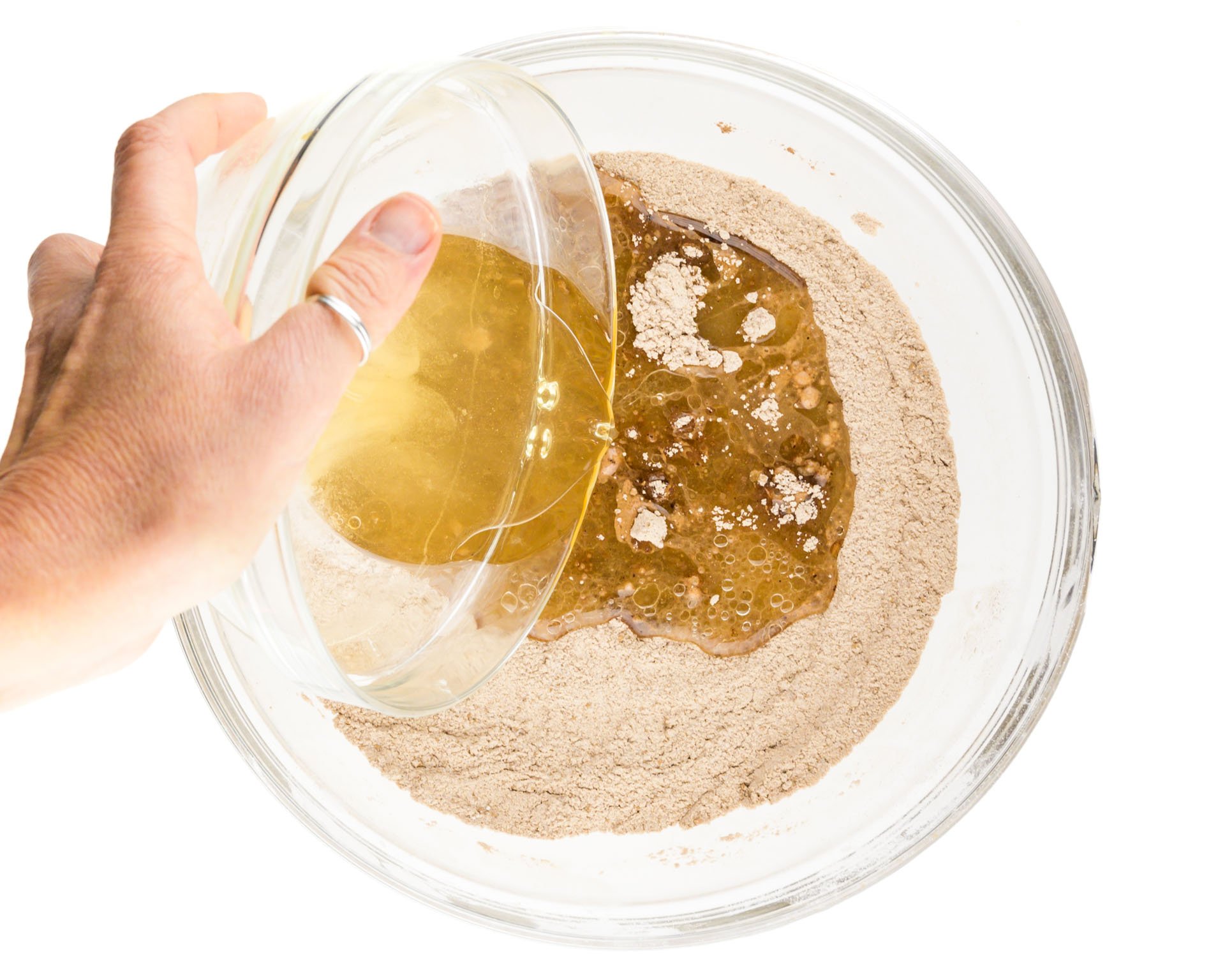 A hand holds a bowl of wet ingredients pouring it into a bowl with cocoa infused flour ingredients.