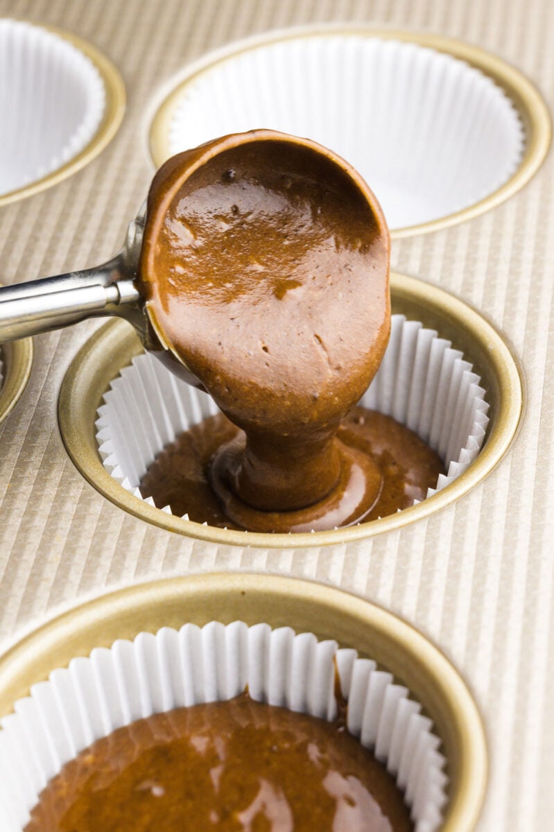 A cookie dough dispenser is pouring cupcake batter in a compartment lined with muffin papers.