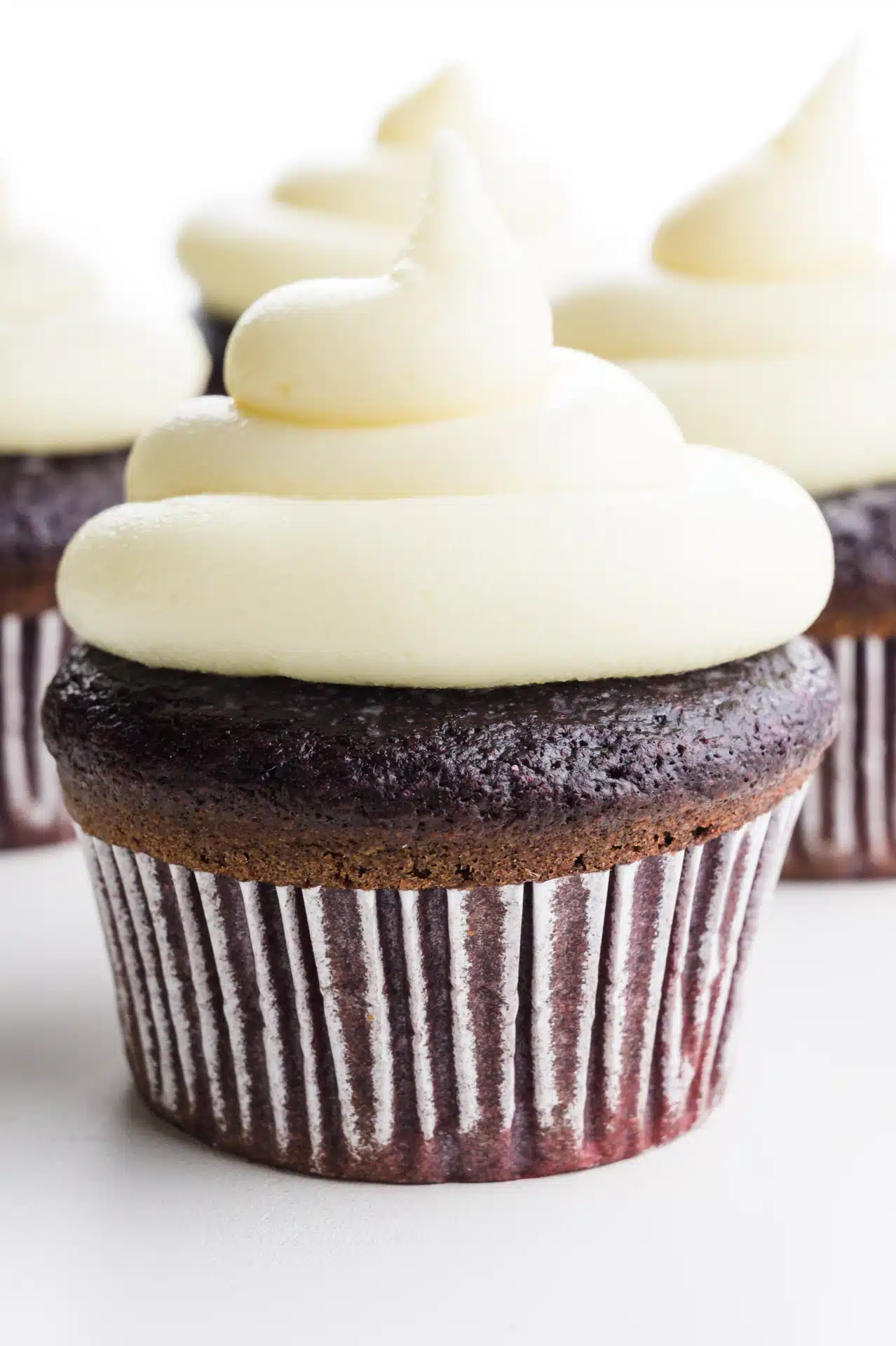 A red velvet cupcake is topped with lots of cream cheese frosting.