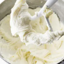 A mixing bowl shows cream cheese frosting in the bowl and on the paddles of the beaters.