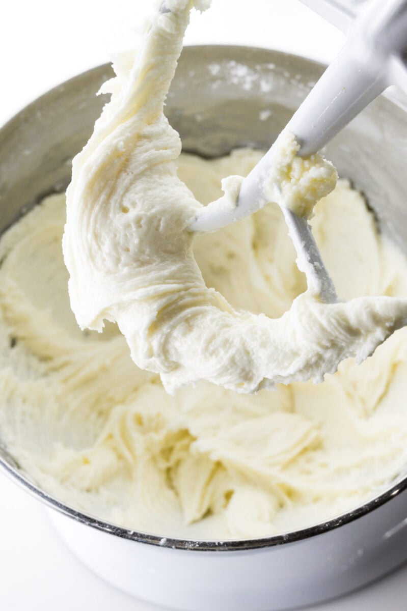 A mixing bowl shows cream cheese frosting in the bowl and on the paddles of the beaters.