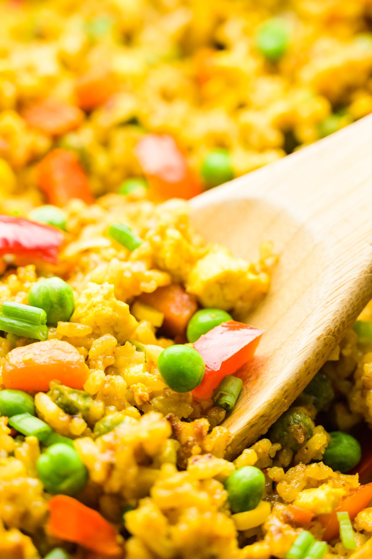 A closeup of a wood spoon in a skillet full of fried rice.