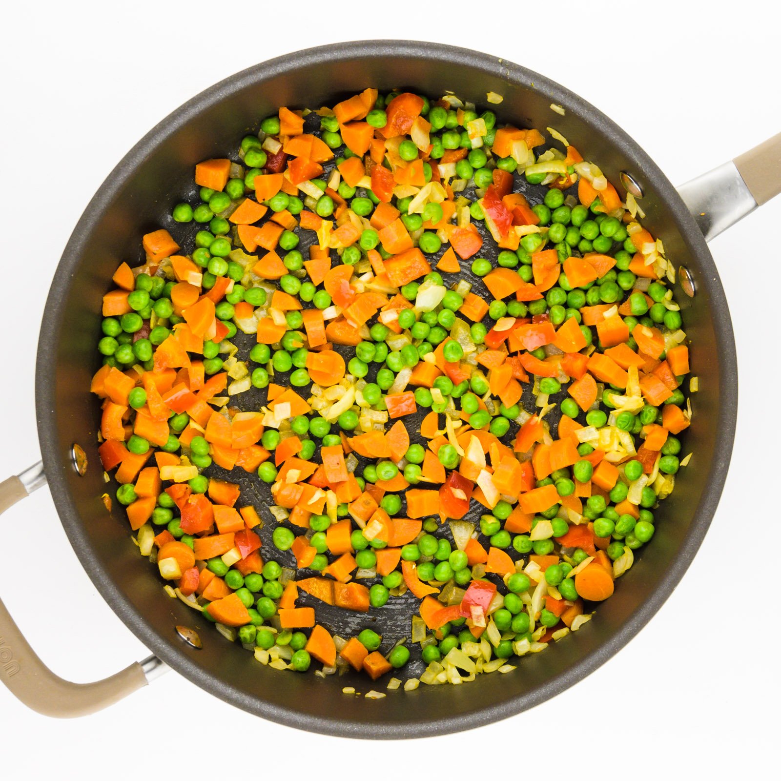 A skillet holds a mixture of vegetables, including peas, carrots, and red bell peppers.
