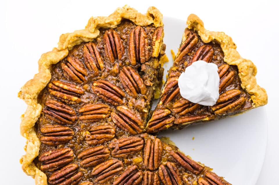 Looking down on a whole pecan pie with a slice cut out and a bit of whipped cream on top.