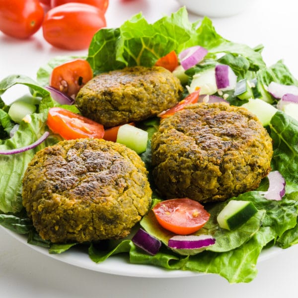 A salad is topped with three falafel patties, with sliced tomatoes, and cucumbers.