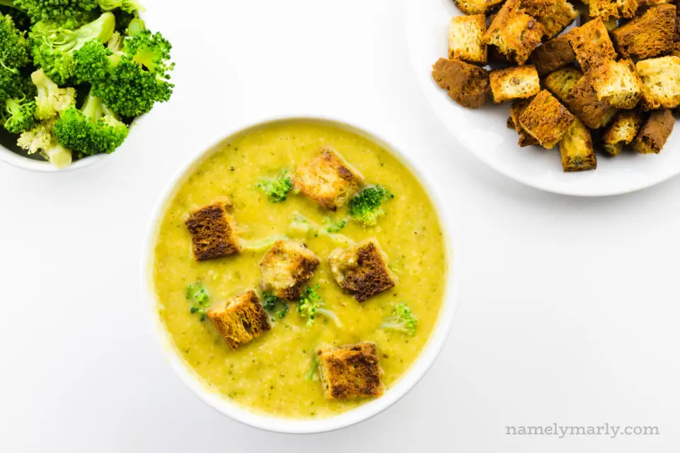 Looking down on a bowl of broccoli soup. A bowl of steamed broccoli and croutons sits beside it.