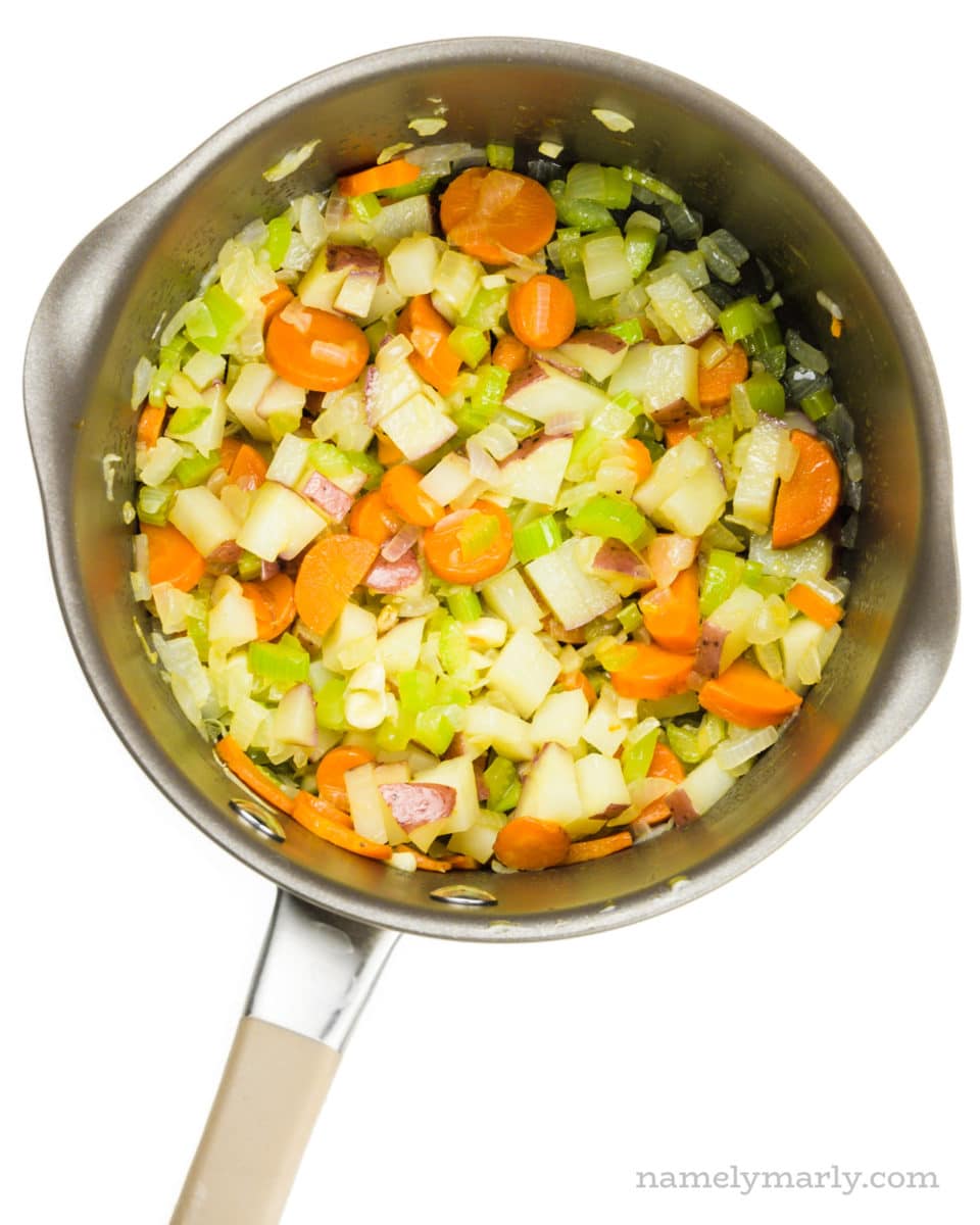 Looking down on a saucepan full of chopped onions, carrots, and celery.
