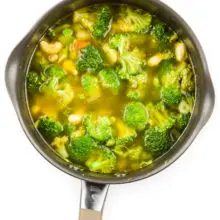 Looking down on a saucepan full of broth, cashews, broccoli, and other veggies.